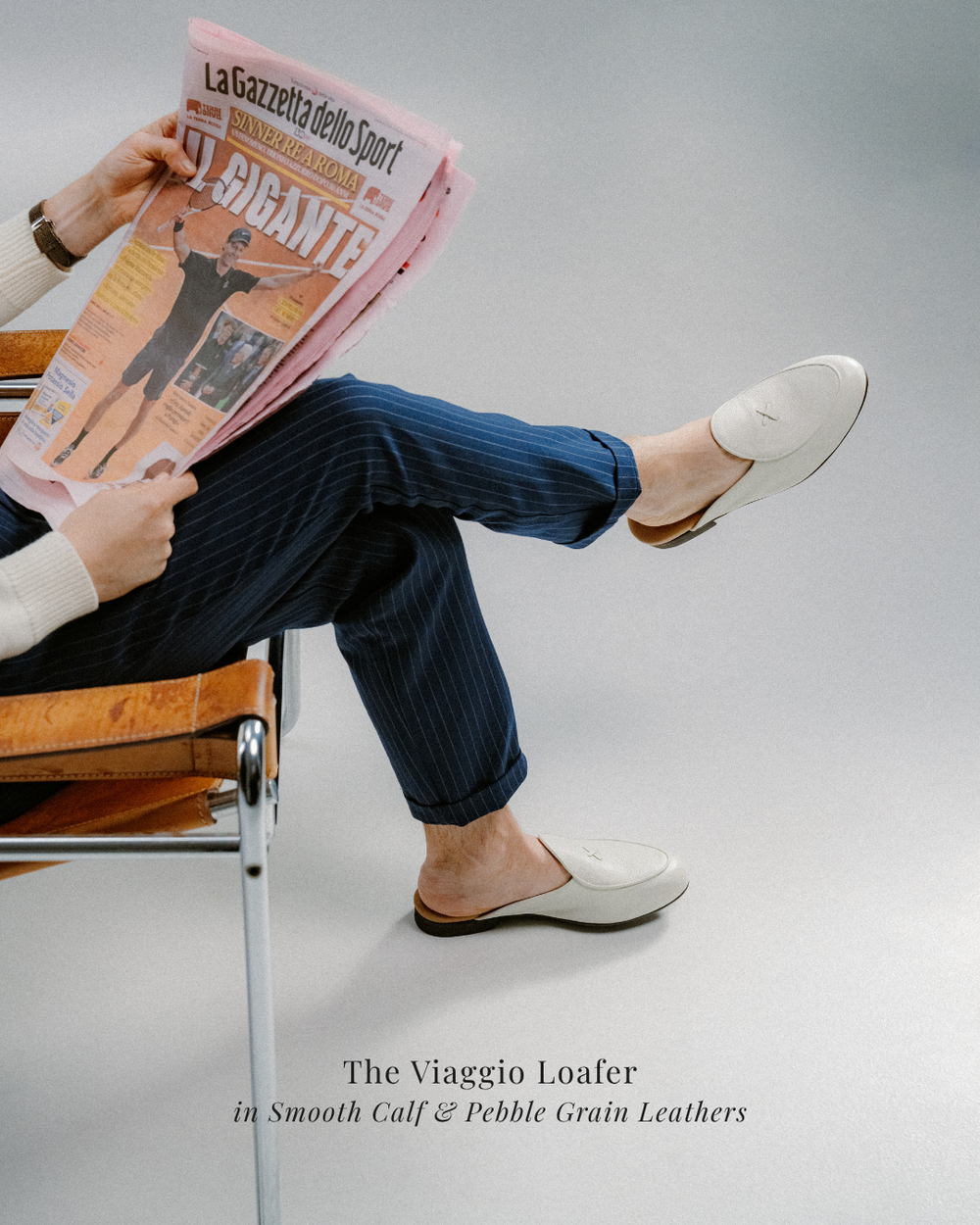man in chair reading newspaper wearing navy striped pants and white backless leather mules