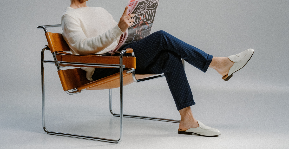 Man in chair wearing white leather backless loafers reading a newspaper