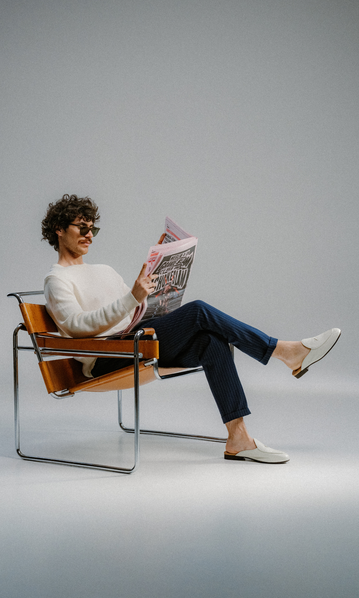 Man in chair wearing white leather backless loafers reading a newspaper