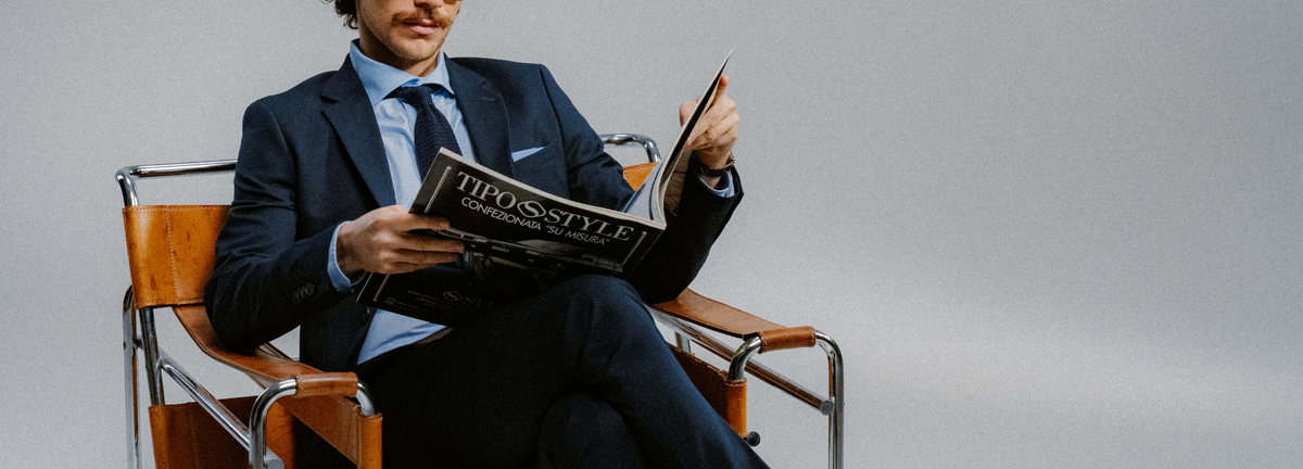man sitting in chair reading magazine wearing a tux and a tie